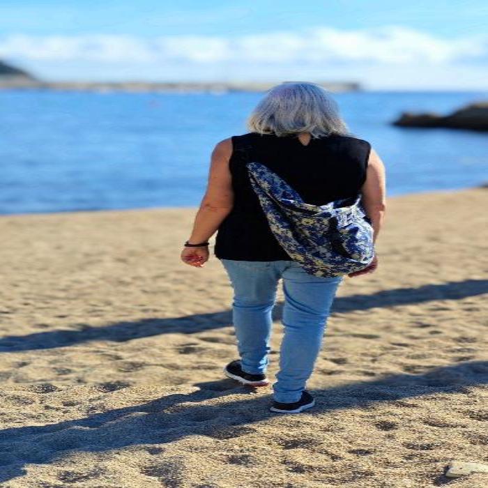 Modelo femenina mostrando el bolso hobo XXL de camuflaje digital azul en un día soleado en la playa. Perfecto para un estilo casual y bohemio.